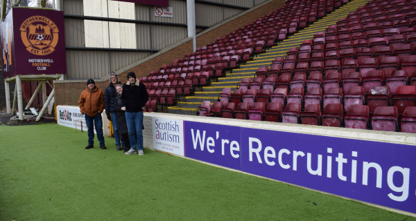 Photograph shows Gary Elliott, Gig Smith, Ailie Paton & Chris Gemmell standing in front of an advertising hoarding at Fir Park which reads 'Scottish Autism We're Hiring'