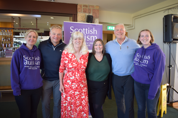 Image is of five people at a golf event, two people are wearing Scottish Autism supporter hoodies