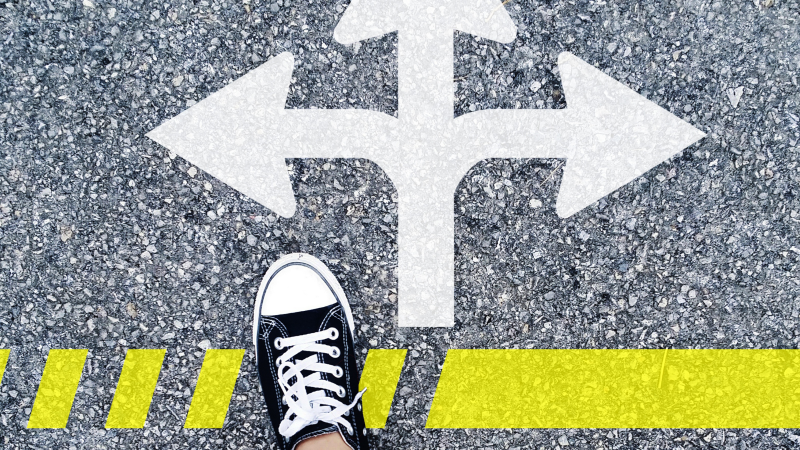 Image is of a person's feet on a road with arrows in many directions