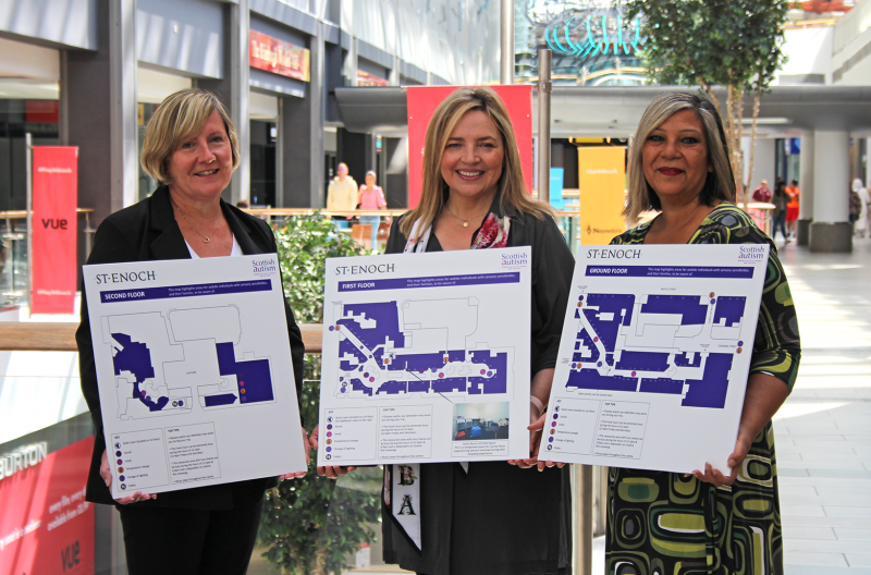 Image is of three people holding boards with a map, shopping centre in background, 