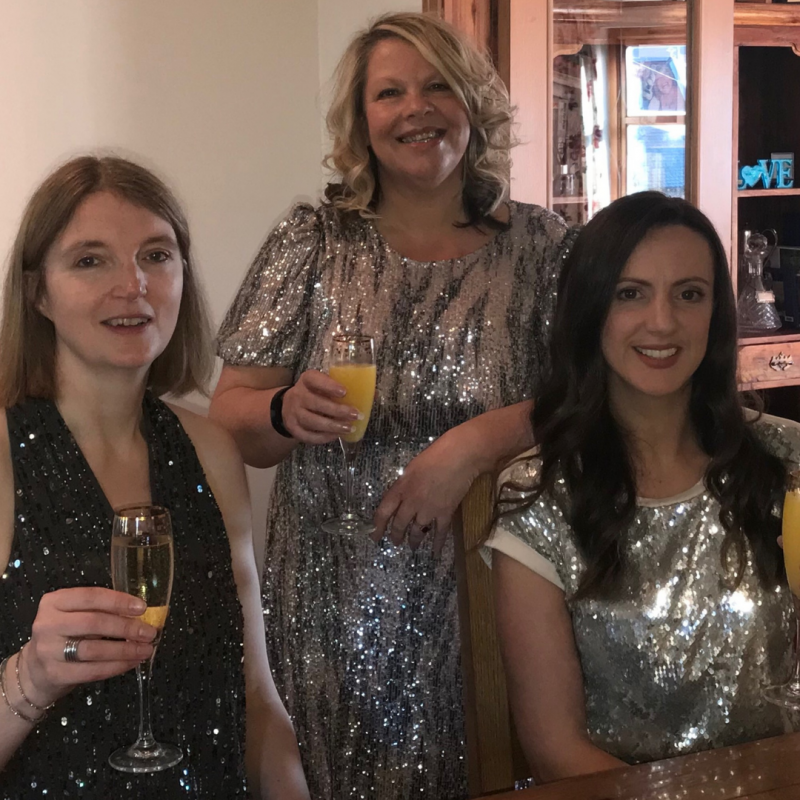 Three people in sparkling dresses, drinks in hand