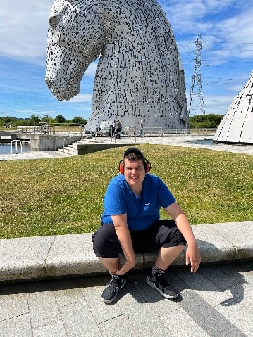 Person sitting next to Kelpies sculpture, outdoors
