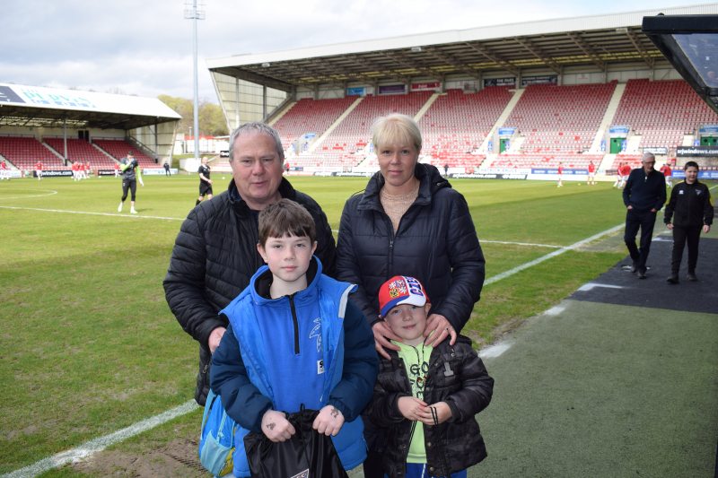 Photograph shows two adults and two children standing beside the pitch in a football stadium