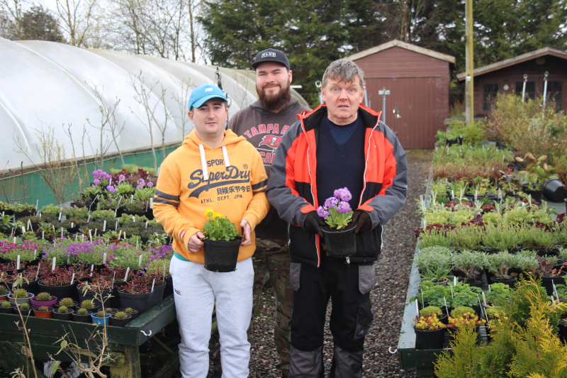 Three people smile while surrounded by plants, garden centre