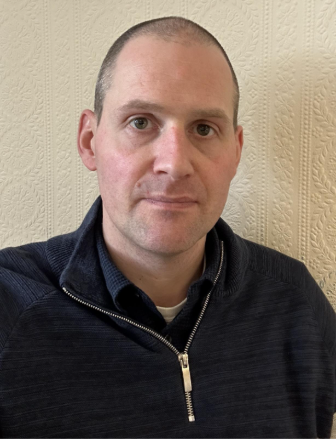 Image is of a person looking at the camera, wearing a dark coloured jumper