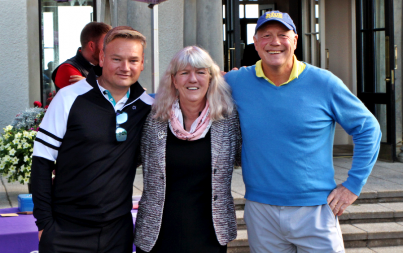 Image shows three people smiling close together, outdoors
