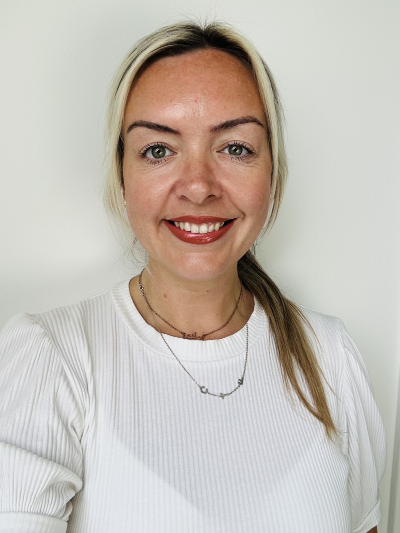 Image of a person with long blond hair in a ponytail, smiling for the camera