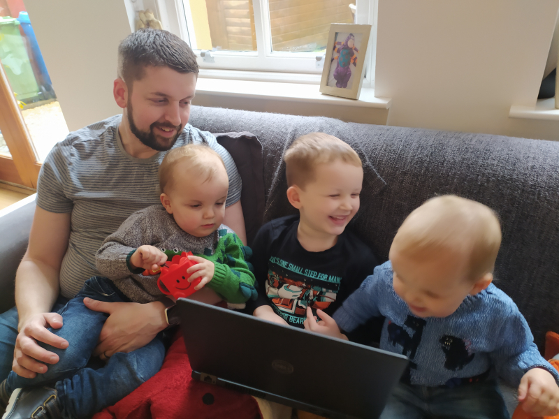 A man and three children sit on a couch, smiling together as they look at a laptop screen
