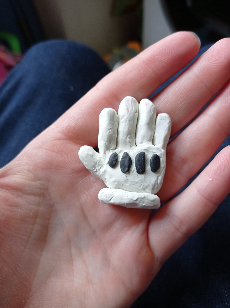 The palm of a hand with a plasticine model of a white glove