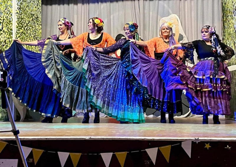 Image is of dancers wearing floaty dresses, on stage, indoors