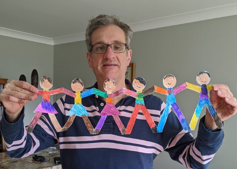 Man smiles as he holds up a colourful people paper chain he's made