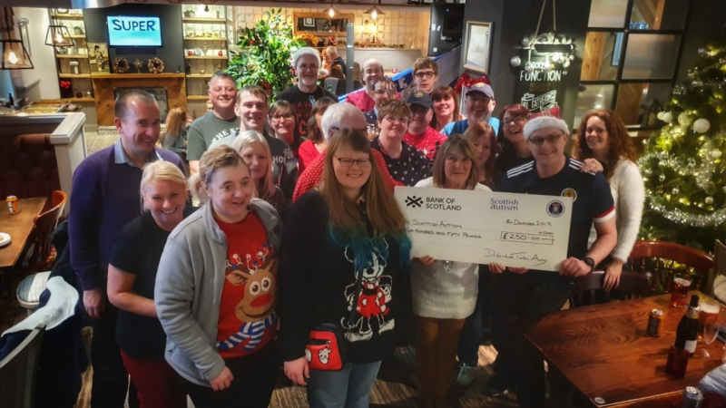 A group of people supported by Scottish Autism attend a Christmas party, holding a cheque for a donation received by the Dunfermline Tartan Army