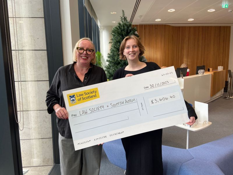 Image of two people in an office holding a fundraising cheque which reads that The Law Society has raised £3,606.40 for the charity Scottish Autism