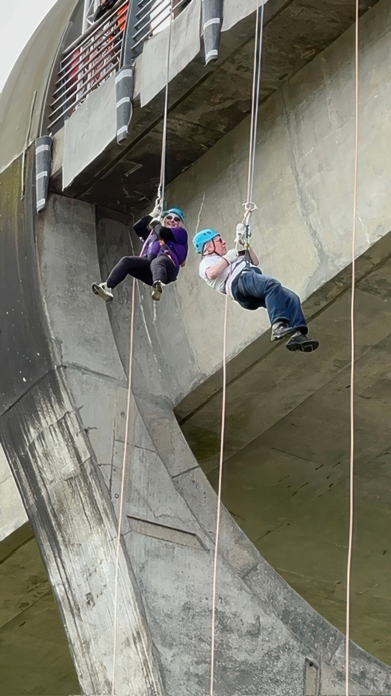 Image is of two people abseiling down a structure, outdoors