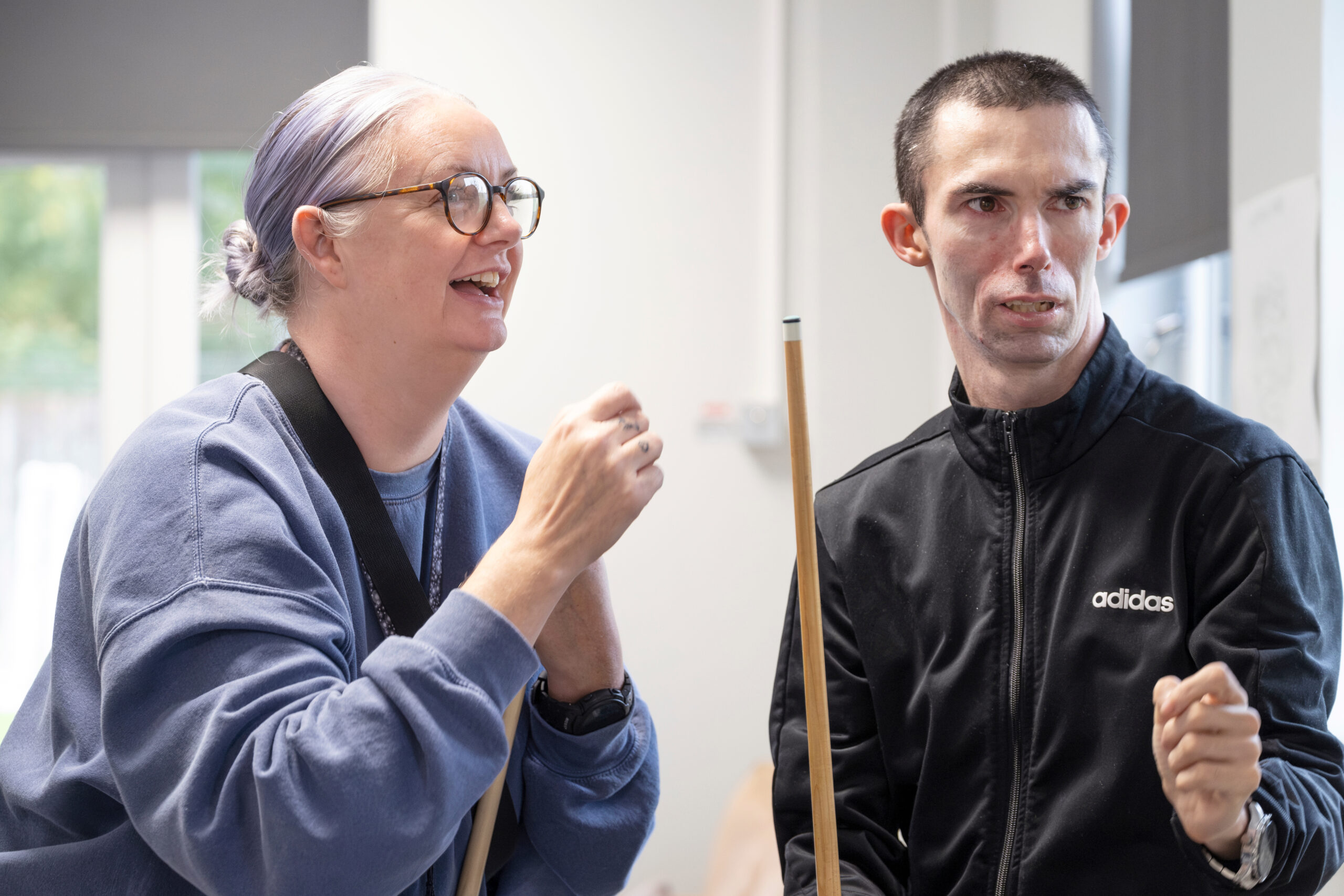 Two people looking across with snooker cues in hand, the female is smiling whilst the male is looking concentrated