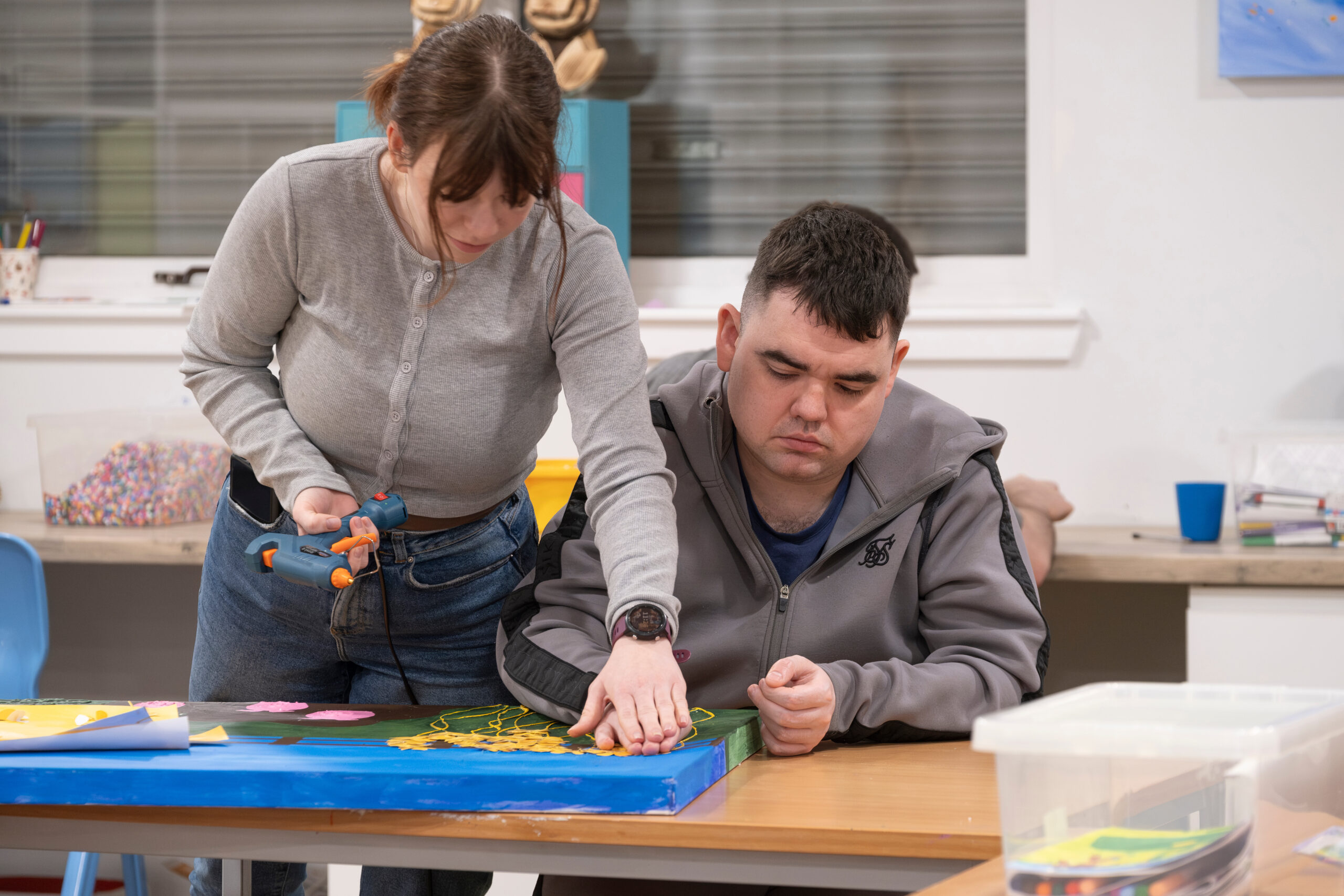 Two adults, working at a table doing arts and crafts