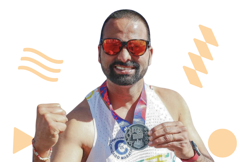 Image is of a runner wearing a vest and sunglasses, fist pumping the air and holding their Chicago marathon medal