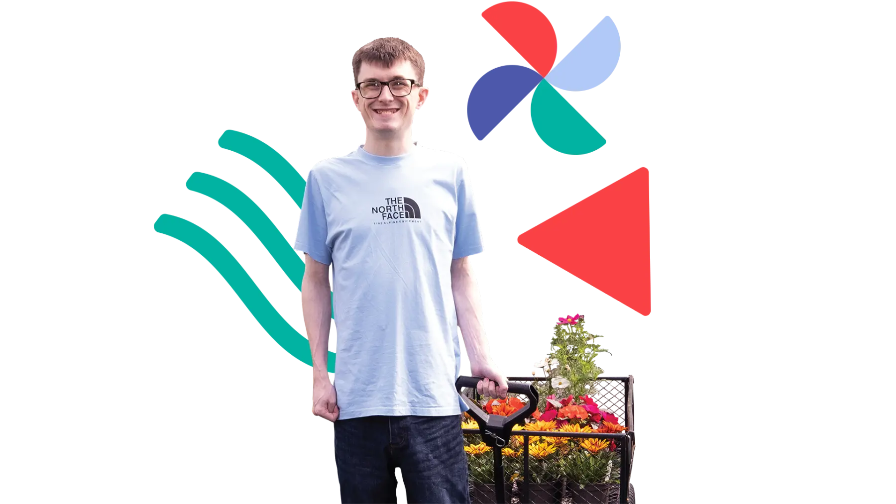 Image is of a young man smiling at the camera and pulling along a cart of plants and colourful flowers