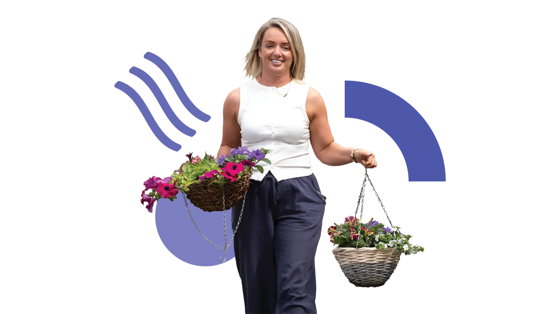 Image is of a woman walking and smiling while carrying a couple of pretty hanging baskets with flowers
