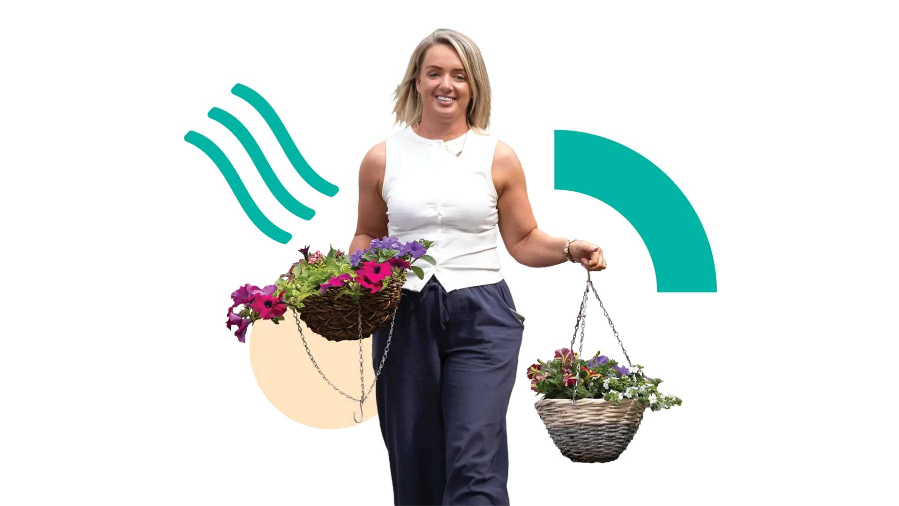 Image is of a woman walking and smiling while carrying a couple of pretty hanging baskets with flowers