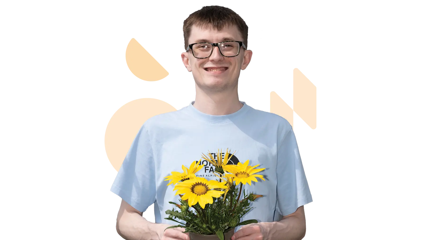 Image is of a young man smiling at the camera and holding a plant with yellow flowers