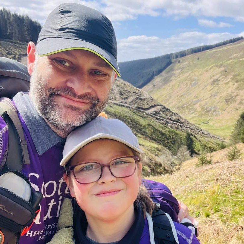 Two Scottish Autism supporters (a father and daughter) smile for the camera with a mountain landscape behind them.