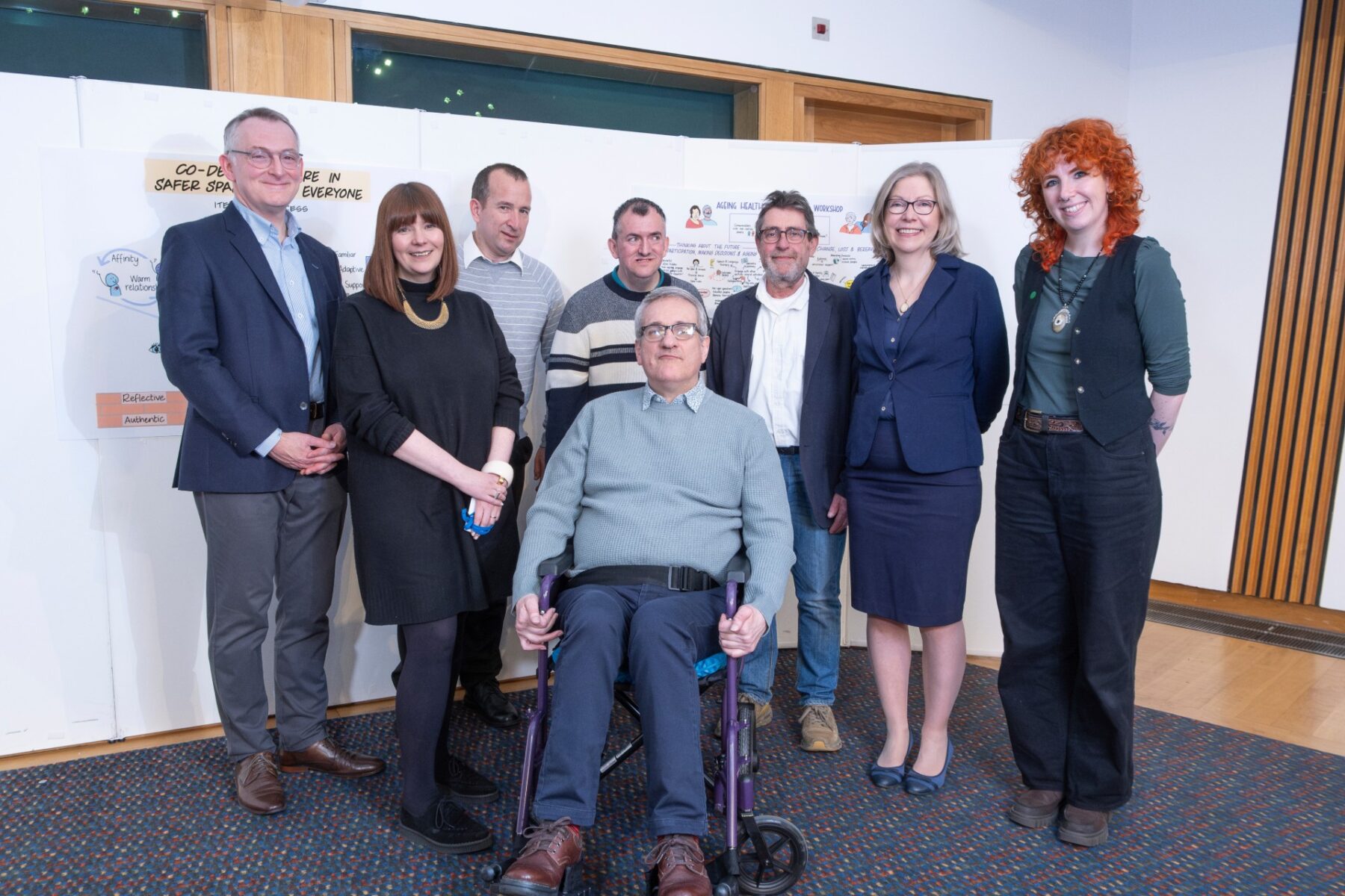Image is a group of eight people smiling for the camera at the Scottish Parliament