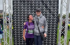 Image is of a runner standing on a podium after finishing and smiling proudly at the other person