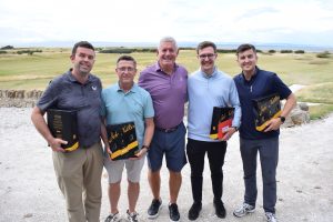 Image is of five golfers standing in front of the course with prizes