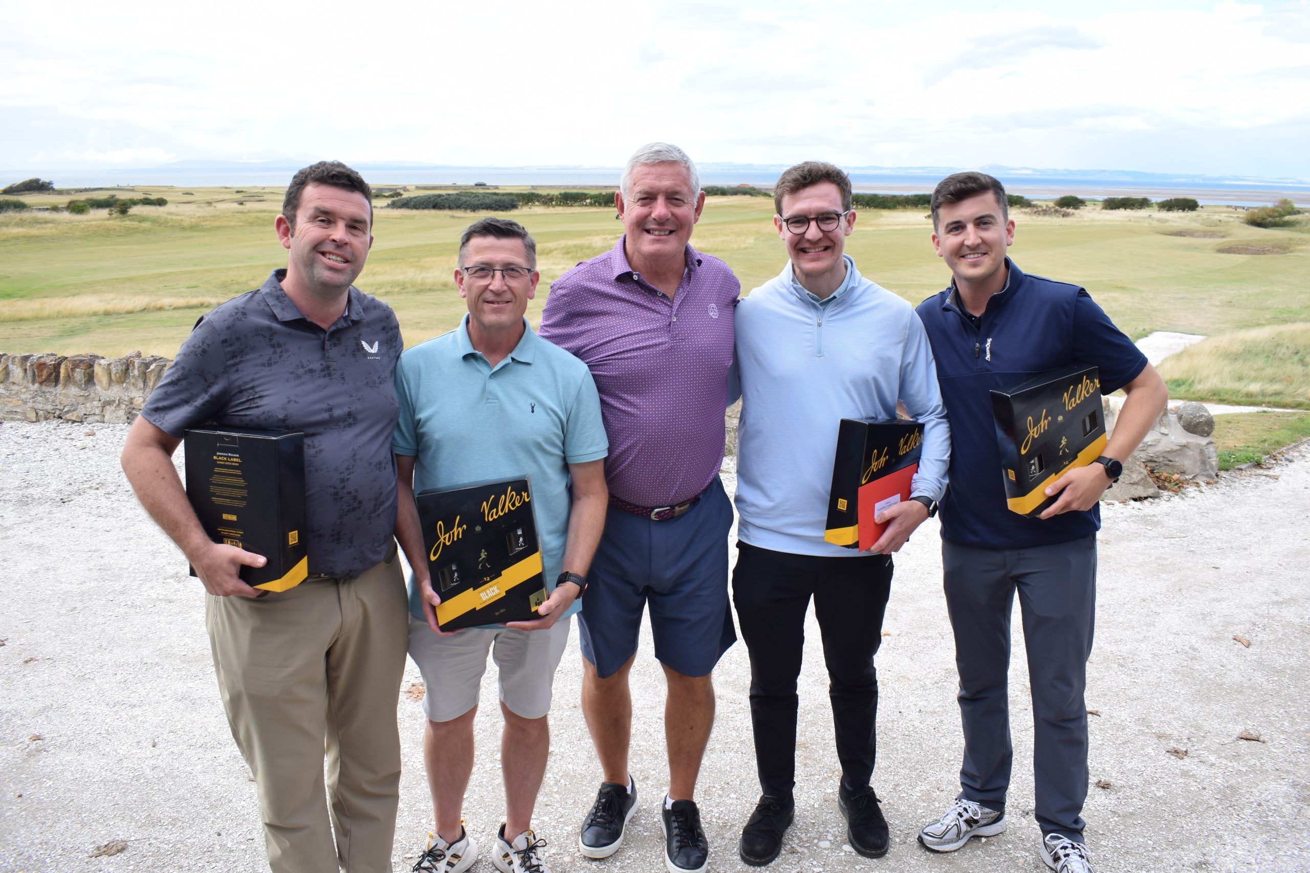 Image is of five golfers standing in front of the course with prizes