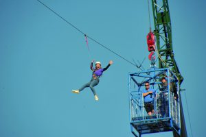 An image of someone zipsliding high up in the sky from a crane, with their hands in the air