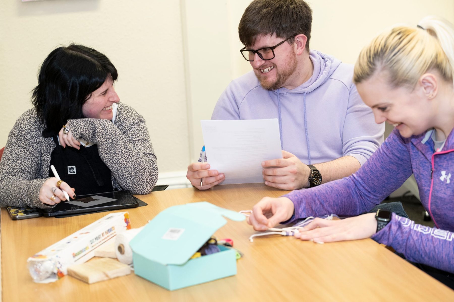 Three people sitting around a table doing crafts.