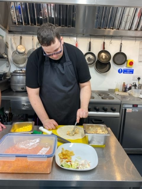 A chef dressed in black prepares a salmon wrap in an industrial kitchen