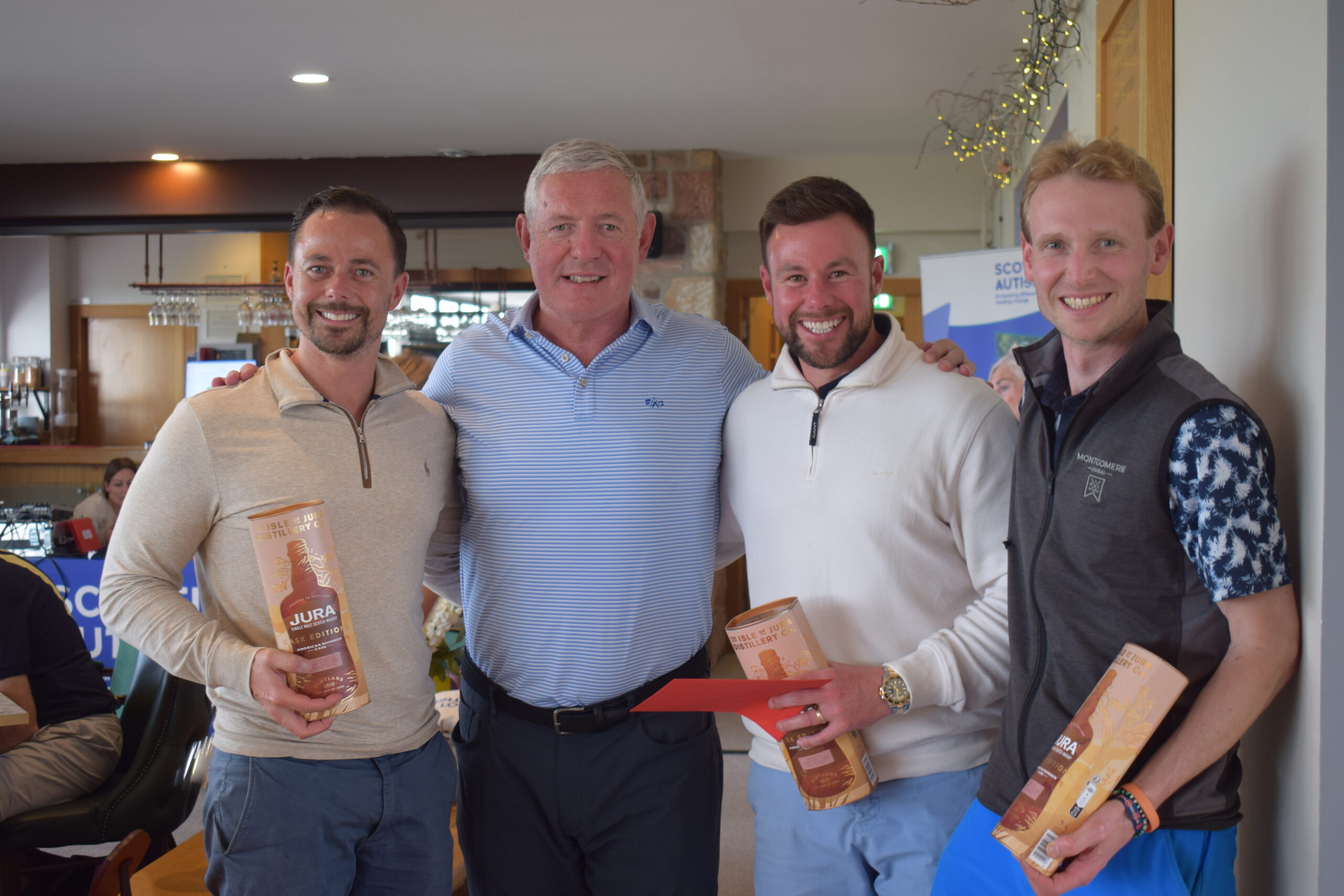 Image is of three people holding trophies and prizes with host Gavin Hastings at Scottish Autism's Golf Day